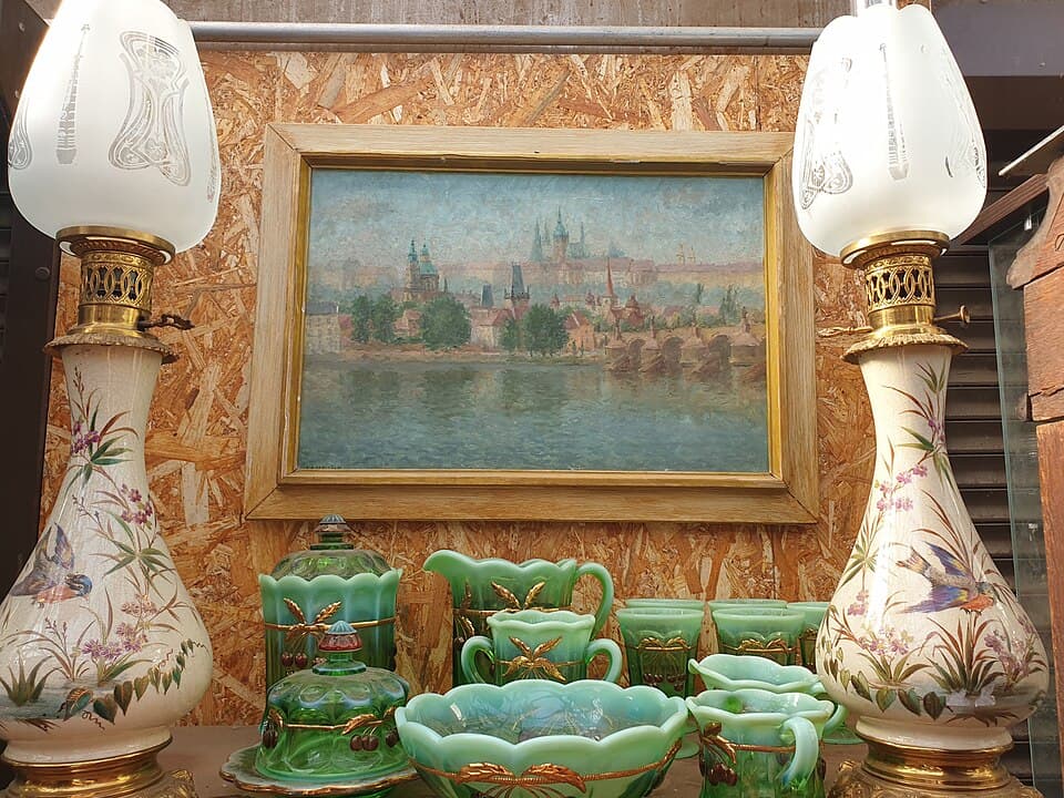Antique lamps, green glassware and a framed painting on a flea market table